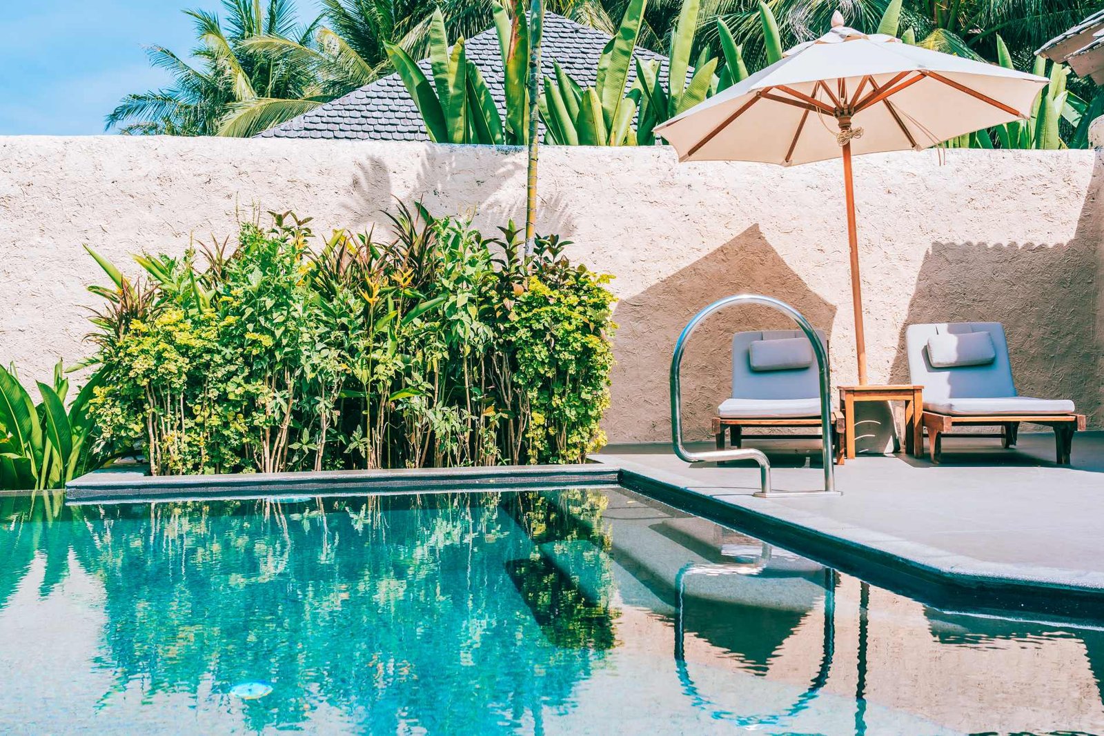 Piscine bleue avec parasol, transats et haie végétale sur une terrasse claire, pisciniste à Brie-Comte-Robert
