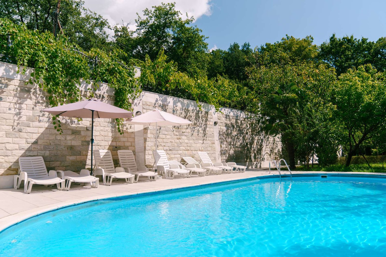 Piscine avec transats et parasols le long d’un mur en pierre ancienne, pisciniste à Melun