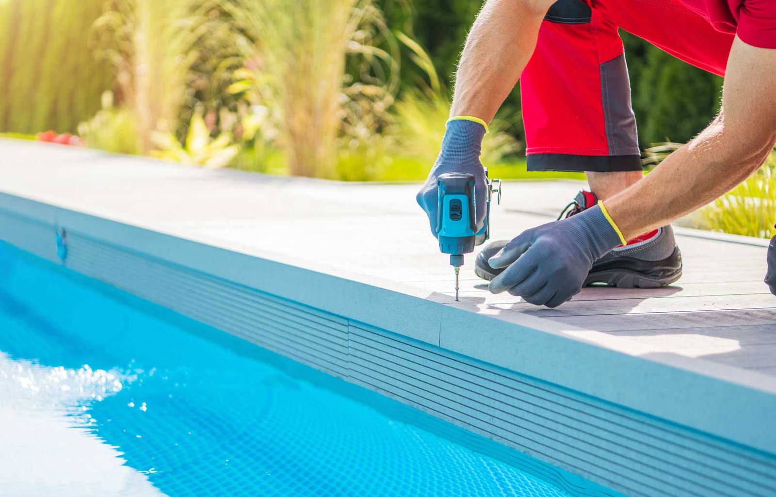 Technicien vissant une lame de terrasse au bord d’une piscine équipée d’un volet immergé